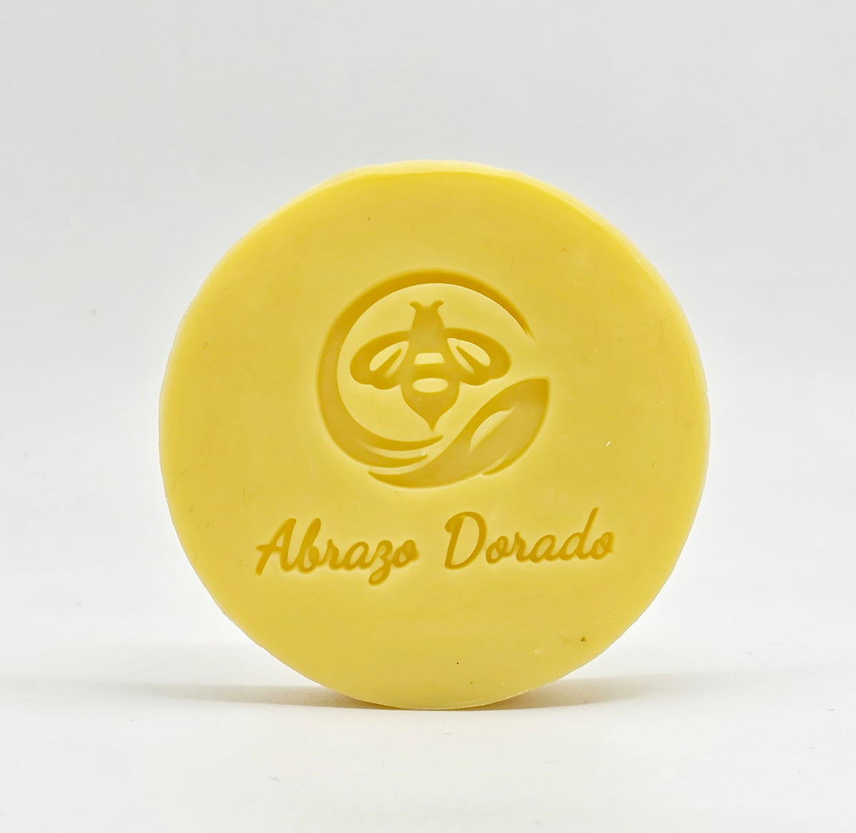 Jabón artesanal de miel Abrazo Dorado con el sello de abeja grabado, sobre fondo claro