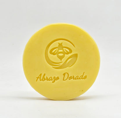 Jabón artesanal de miel Abrazo Dorado con el sello de abeja grabado, sobre fondo claro