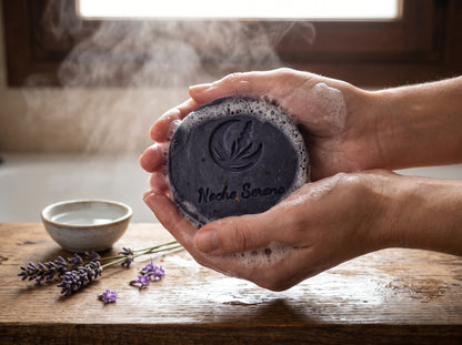 Manos haciendo espuma con un jabón artesanal de lavanda frente a una ventana con luz suave y vapor, junto a ramitas de lavanda y un cuenco de cerámica