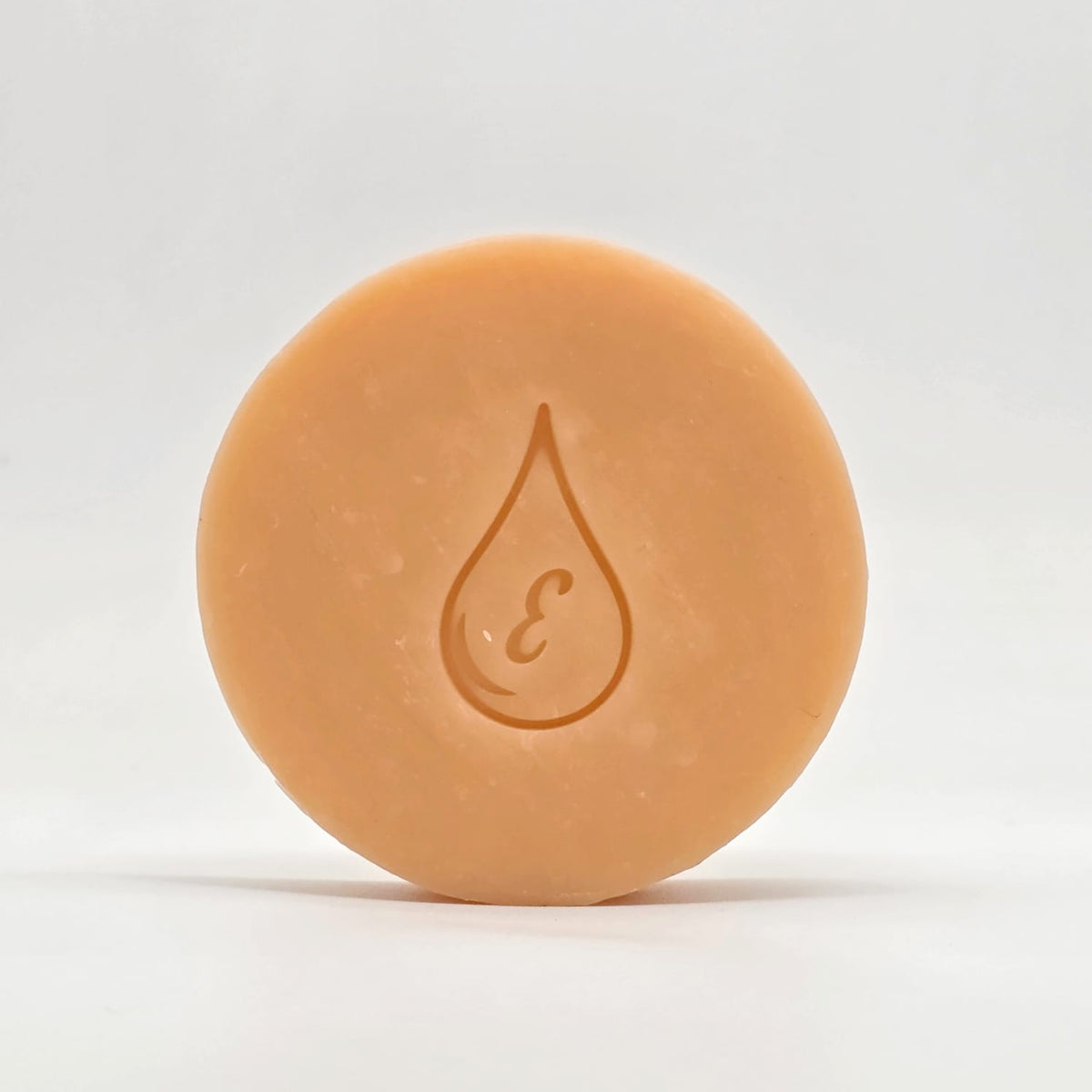 Jabón artesanal de Vitamina E, de color durazno, con el sello de gota con la letra E grabado, sobre fondo claro