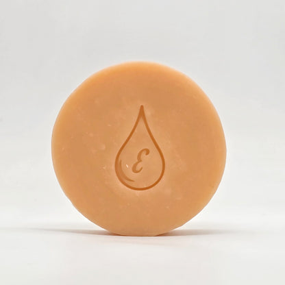Jabón artesanal de Vitamina E, de color durazno, con el sello de gota con la letra E grabado, sobre fondo claro