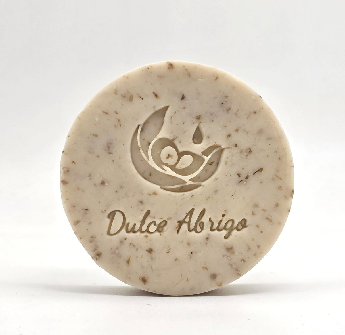 Jabón artesanal de avena y coco Dulce Abrigo con el sello grabado y trocitos de avena, sobre fondo claro