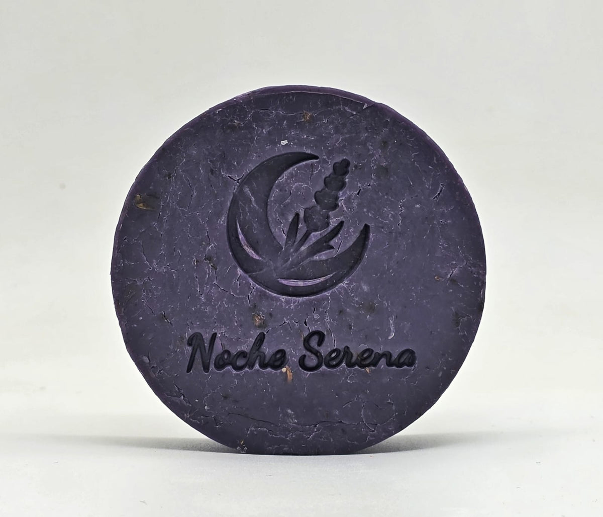 Jabón artesanal de lavanda Noche Serena con el sello de luna y lavanda grabado, sobre fondo gris claro